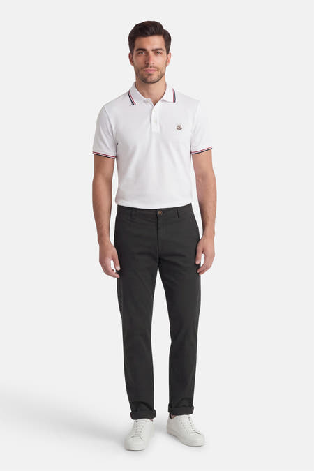 Zwarte chino van Jack & Jones Jeans Intelligence, met lange pijpen en opgerolde zoom, gecombineerd met een wit poloshirt en witte sneakers.