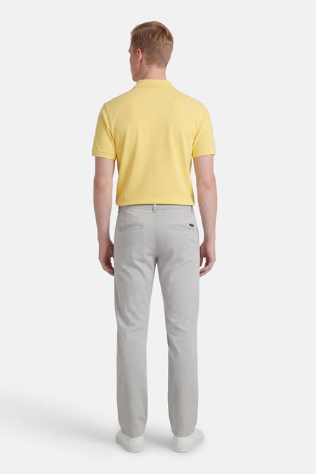 Grijze chino van JACK & JONES JEANS INTELLIGENCE, gezien van achteren, gecombineerd met een geel poloshirt en witte schoenen.
