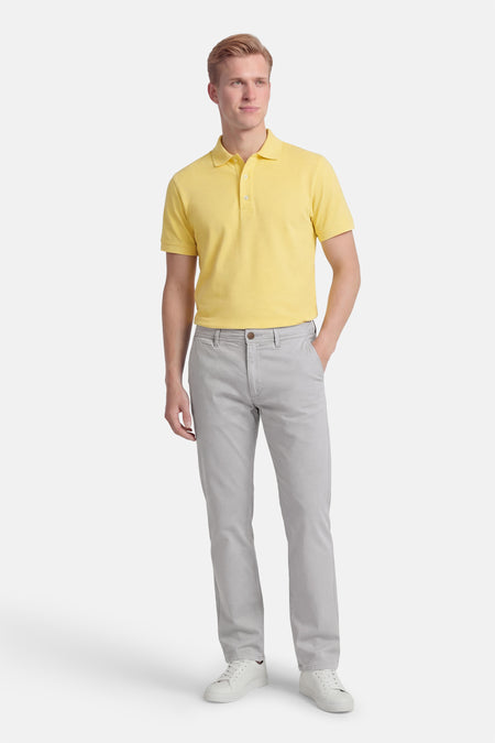 Grijze chino van JACK & JONES JEANS INTELLIGENCE, gecombineerd met een geel poloshirt en witte sneakers.