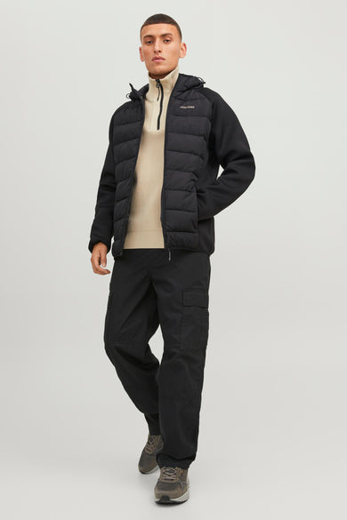 Doudoune noire à capuche de CORE BY JACK & JONES, design matelassé, modèle portant un pull beige et un pantalon cargo noir, vue de face