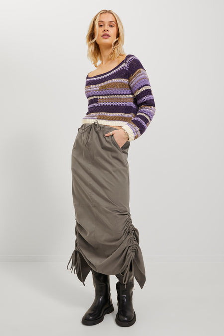 Bruine rok van JJXX, met drawstring taille en geplooide details aan de zijkanten, gecombineerd met een gestreepte trui en zwarte laarzen.
