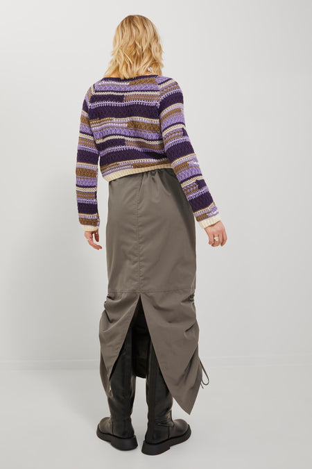 Jupe brune de JJXX, avec une longueur longue et fendue à l'arrière, portée avec des bottes noires et un pull rayé.