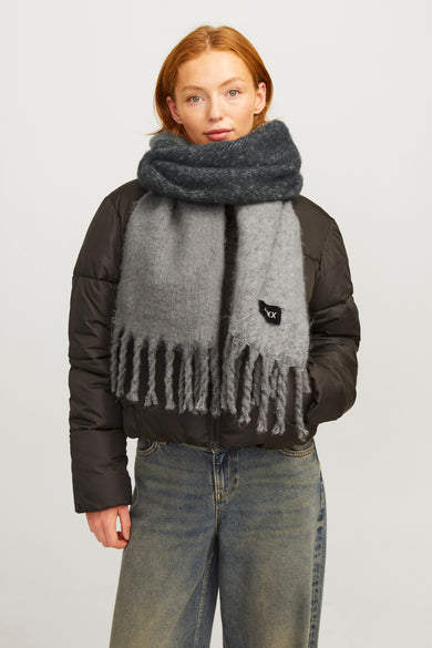 Chapeau d'hiver gris de JJXX, avec franges, porté avec une veste en laine noire et des jeans bleus.
