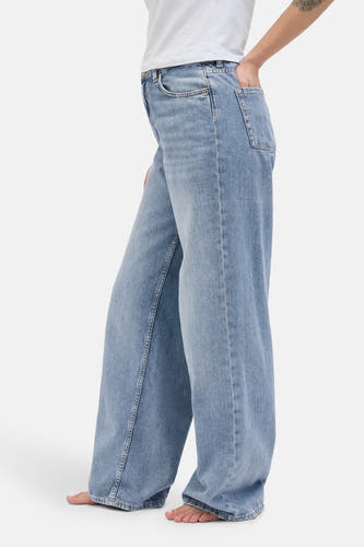 Lichtblauwe wijde jeans van JJXX, met een hand in de zak en een witte top.
