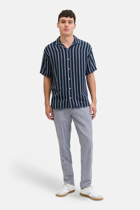 Blauwe chino van JACK & JONES JEANS INTELLIGENCE, gedragen met een gestreept overhemd en witte sneakers.