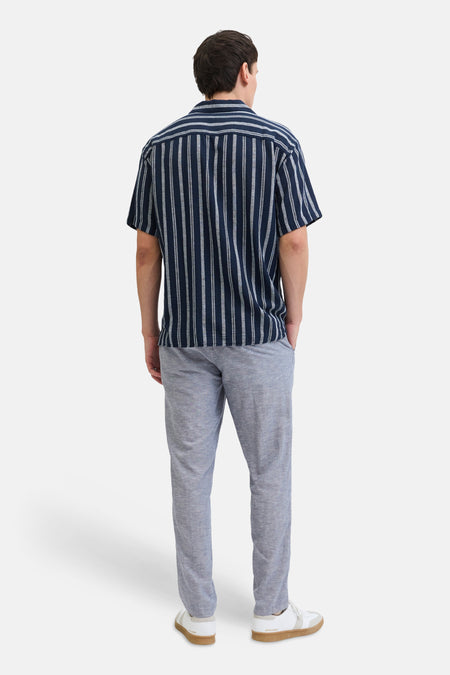 Blauwe chino van JACK & JONES JEANS INTELLIGENCE, met een lichte textuur, gecombineerd met een gestreept overhemd en witte sneakers.
