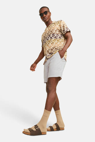 Beige short van JACK & JONES JEANS INTELLIGENCE, gecombineerd met een overhemd met bloemenprint en bruine sandalen met sokken.
