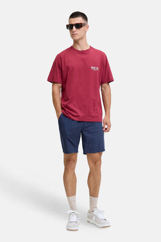 Blauwe short van JACK & JONES JEANS INTELLIGENCE, gedragen door een man met rood T-shirt, zonnebril en witte sneakers.
