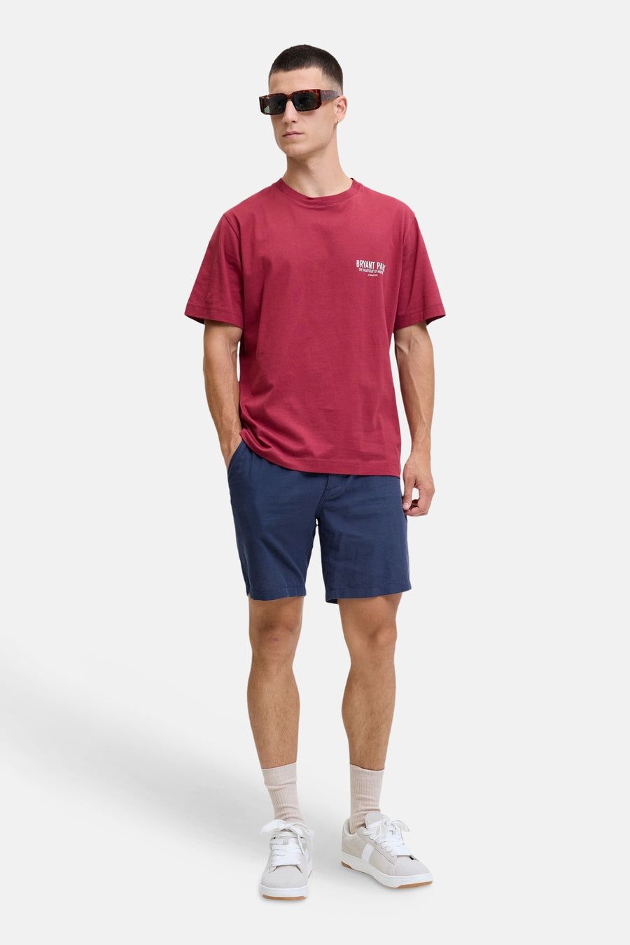 Blauwe short van JACK & JONES JEANS INTELLIGENCE, gedragen door een man met rood T-shirt, zonnebril en witte sneakers.