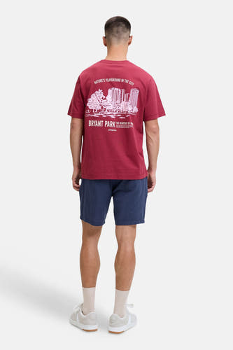 Blauwe short van JACK & JONES JEANS INTELLIGENCE, gedragen door een man met een bordeauxrood T-shirt met witte print en beige sneakers, van achteren gezien.