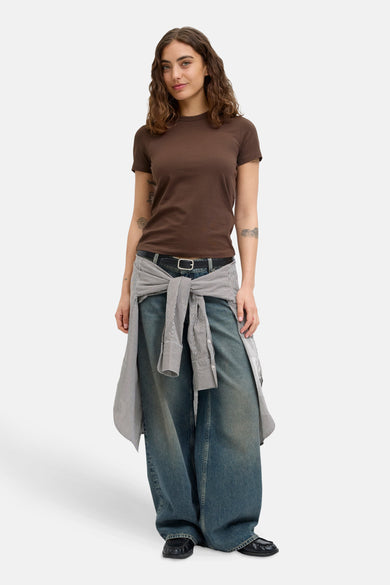 Bruin T-shirt met korte mouwen van JJXX, met tattoos op de armen, gecombineerd met wijde jeans en een gestreept overhemd om de taille.
