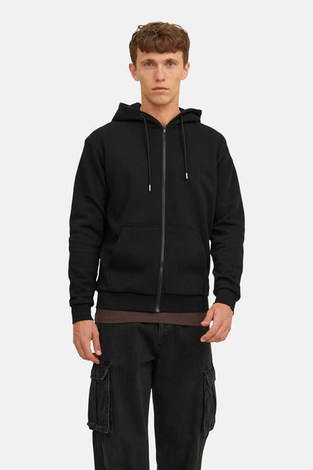 Zwarte sweater van CORE BY JACK & JONES, met rits en capuchon, gedragen over een bruin shirt en zwarte cargo broek.
