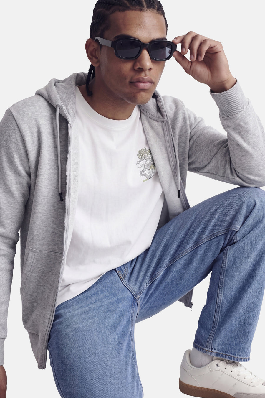 Grijze zip hoodie van CORE BY JACK & JONES, met capuchon en voorzak, gedragen over wit T-shirt met draakprint, blauwe jeans en witte sneakers, lifestyle shot.