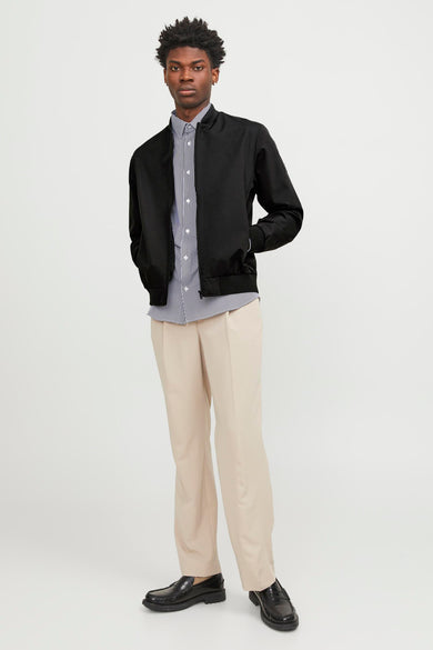 Zwarte korte jas van PREMIUM by JACK & JONES, gedragen over een gestreept overhemd en crèmekleurige pantalon.
