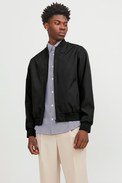 Zwarte korte jas van PREMIUM by JACK & JONES, gedragen over een gestreept overhemd en beige pantalon.

