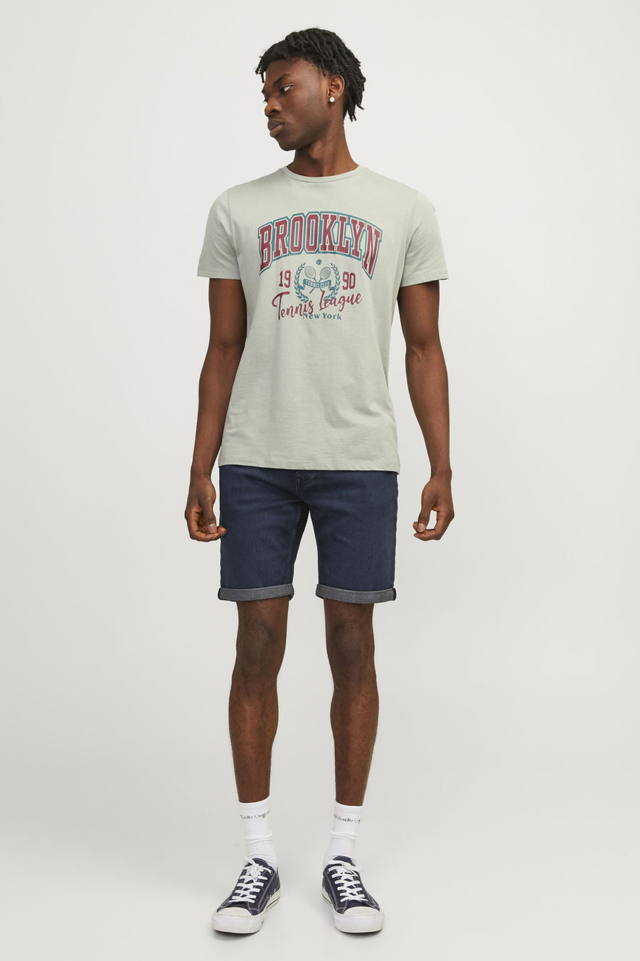 Een man in een grijze T-shirt met "Brooklyn" en donkerblauwe korte broek.