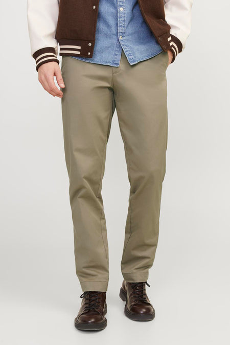 Beige chino van JACK & JONES JEANS INTELLIGENCE, gedragen met een denim overhemd, varsity jacket en bruine veterschoenen.