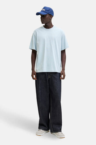 Blauw T-shirt met korte mouwen van CORE BY JACK & JONES, gedragen met een blauwe pet en wijde jeans, met witte sneakers.
