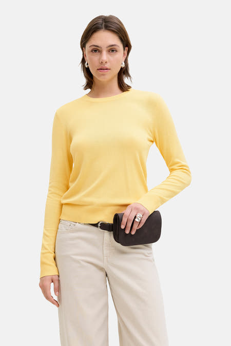 Gele trui met ronde hals van JJXX, gedragen met een bruine riemtas en crèmekleurige broek.
