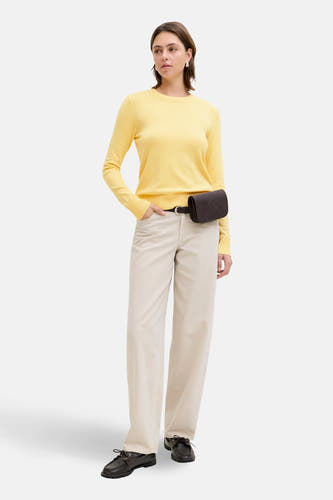 Gele trui met ronde hals van JJXX, gecombineerd met een bruine fannypack en beige broek.