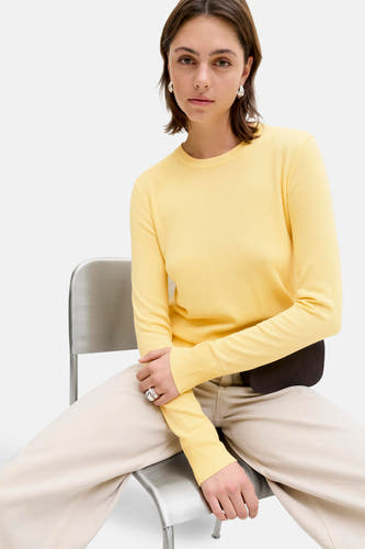 Pull jaune à col rond de JJXX, porté avec un pantalon beige et des bagues argentées, assis sur une chaise en métal.