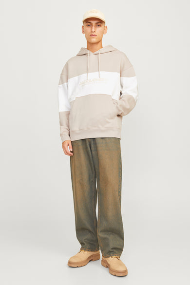 Man in hoodie met kleurblokken, jeans en suède schoenen.