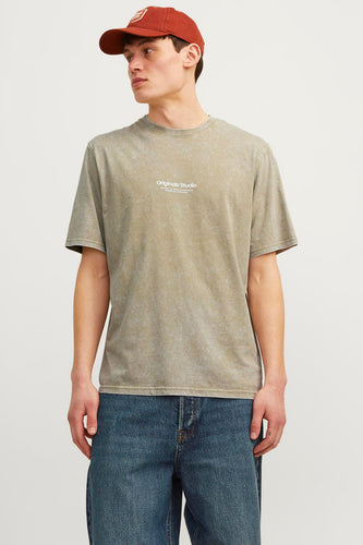 Man met bruine pet, beige T-shirt met print en blauwe jeans.
