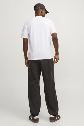 T-shirt blanc à manches courtes d'ORIGINALS BY JACK & JONES, porté par un homme avec un pantalon foncé et des chaussures marrons.