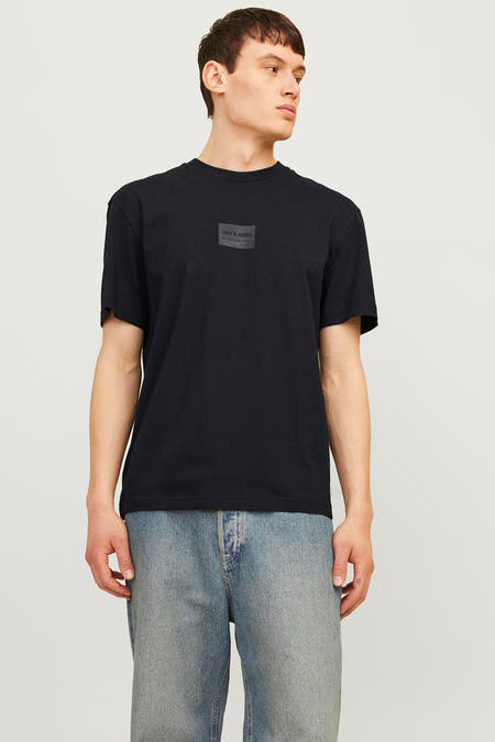 T-shirt noir à manches courtes de CORE BY JACK & JONES, porté avec des jeans bleus et des baskets blanches.