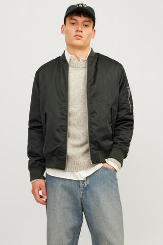 Groene korte jas van CORE BY JACK & JONES, gedragen over een grijze trui, witte blouse en blauwe jeans met pet.