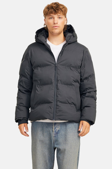 Zwarte regenjas van CORE BY JACK & JONES, met capuchon, gedragen over een wit T-shirt en een blauwe jeans.