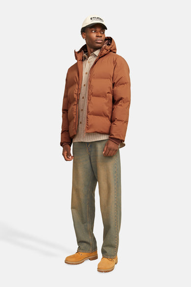Bruine regenjas van CORE BY JACK & JONES, gedragen met een geruit overhemd, losse jeans en suède schoenen.