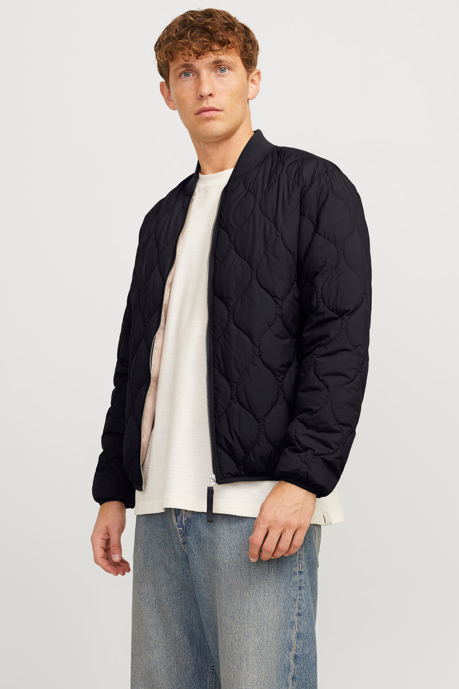 Zwarte korte jas van PREMIUM BLUE by JACK & JONES, met een gewatteerd ruitpatroon, gedragen met een crèmekleurig shirt en blauwe jeans.
