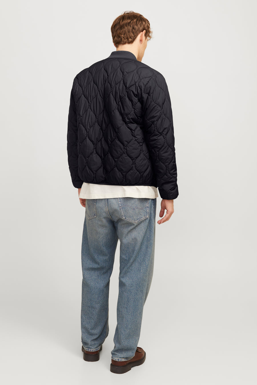 Zwarte korte jas van PREMIUM BLUE by JACK & JONES, met doorgestikt ruitpatroon en gedragen met een wit shirt en blauwe jeans.

