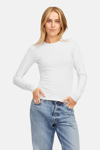 T-shirt blanc à manches longues de JJXX, porté avec des jeans et des ballerines noires, devant un fond blanc.