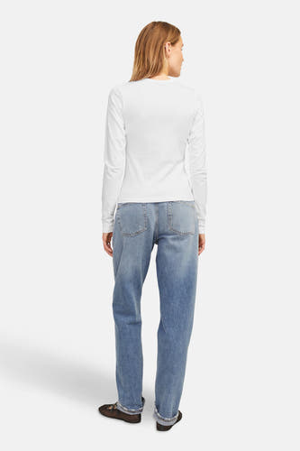T-shirt blanc à manches longues de JJXX, avec un dos simple et droit, associé à des jeans bleus et des chaussures noires.