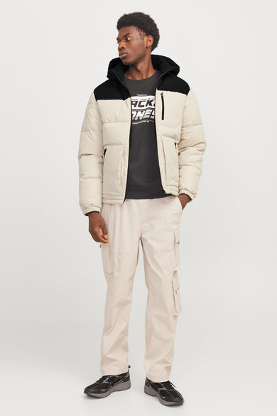 Korte ecru jas van CORE BY JACK & JONES, met zwarte details en gedragen met beige cargobroek en zwarte sneakers.
