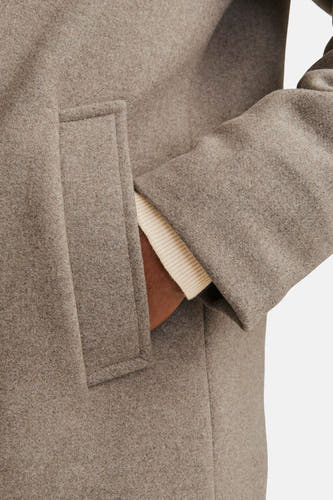 Beige lange jas van PREMIUM by JACK & JONES, met een hand in de zak en een crèmekleurige trui eronder.
