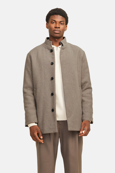Beige lange jas van PREMIUM by JACK & JONES, met knoopsluiting en een witte trui eronder.
