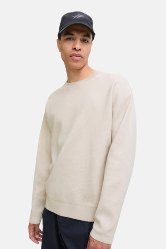 Beige trui met ronde hals van PREMIUM by JACK & JONES, gedragen met een zwarte pet en donkere broek.
