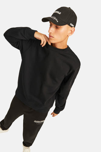 Zwarte sweater met ronde hals van ORIGINALS BY JACK & JONES, gedragen met een zwarte pet en zwarte joggingbroek.
