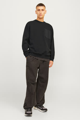 Zwarte sweater van CORE BY JACK & JONES, met borstzak en gedragen met donkere broek en sneakers.