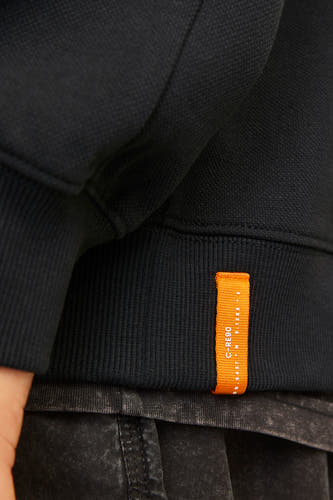 Zwarte sweater van CORE BY JACK & JONES met een kleine oranje merklabel aan de zijkant.