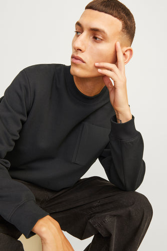 Zittende man in zwarte sweater en broek.