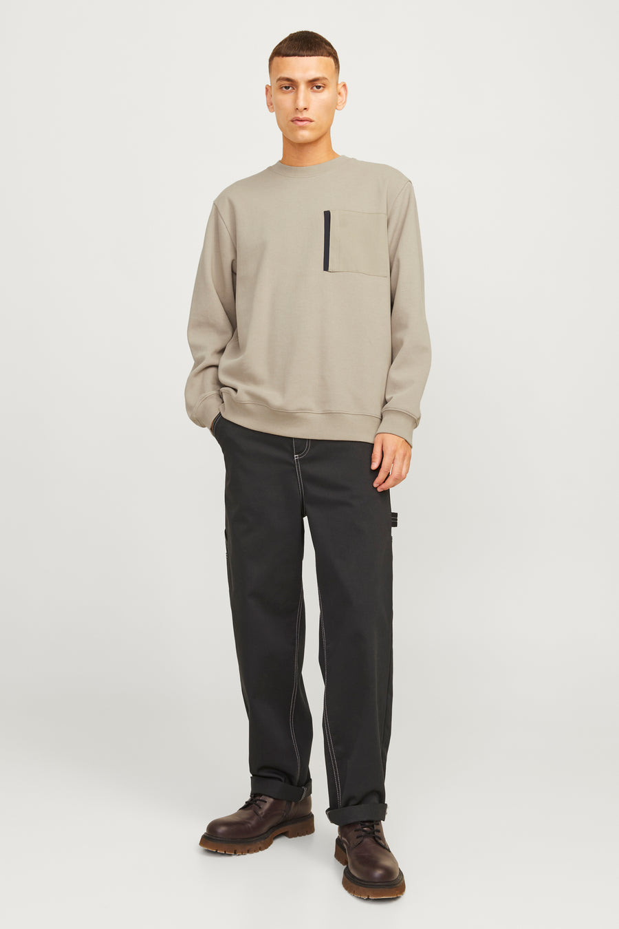 Man in beige sweater, zwarte broek en bruine schoenen.