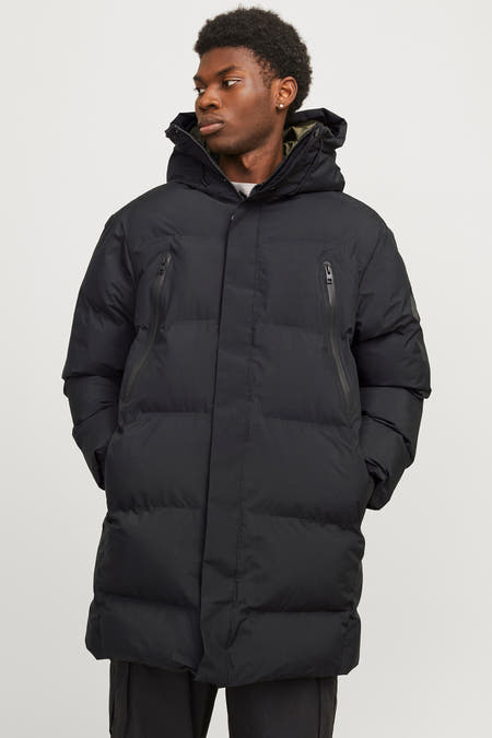 Zwarte lange jas van CORE BY JACK & JONES met ritszakken en capuchon, gedragen met een broek.