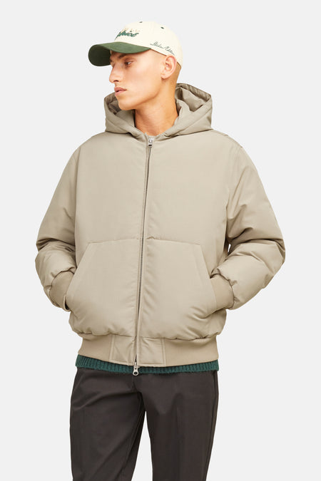 Veste courte beige de CORE BY JACK & JONES avec motif à carreaux subtil, capuche, fermeture éclair, poignets côtelés et poches latérales, portée par un mannequin avec une casquette.