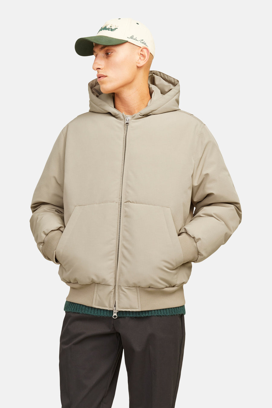 Beige korte jas van CORE BY JACK & JONES met subtiel rasterpatroon, capuchon, rits, geribde boorden en steekzakken, gedragen door een model met een pet.