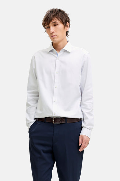 Chemise blanche à manches longues de PREMIUM by JACK & JONES, avec fermeture boutonnée visible et portée avec un pantalon bleu foncé et une ceinture en cuir.