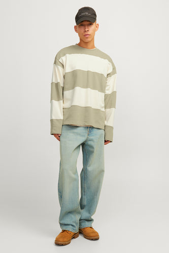 Man met gestreept shirt, wijde jeans en bruine schoenen, tegen een witte achtergrond.